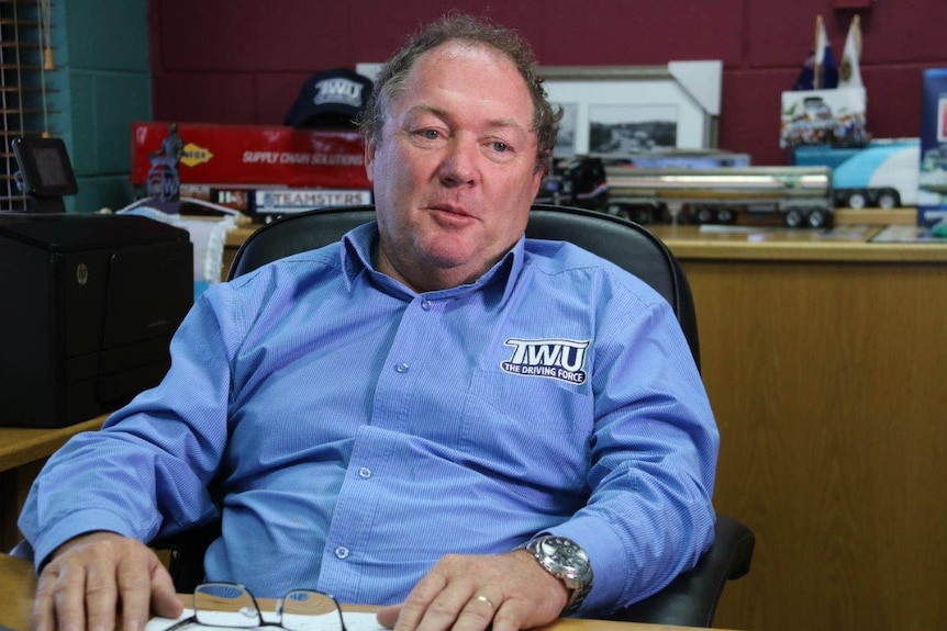 A man in an office chair, wearing a blue button-up shirt with a TWU logo, with models of trucks behind him.
