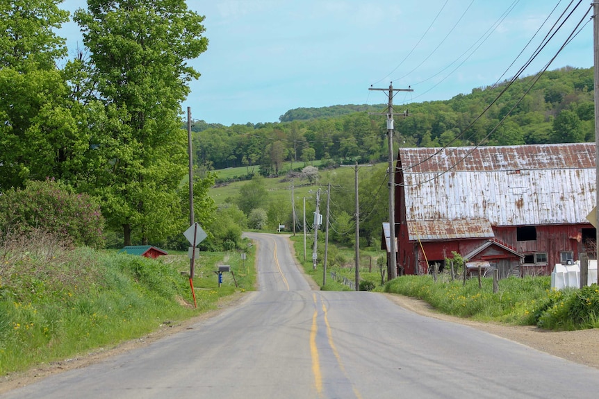A red barn, a road, and rolling green hills