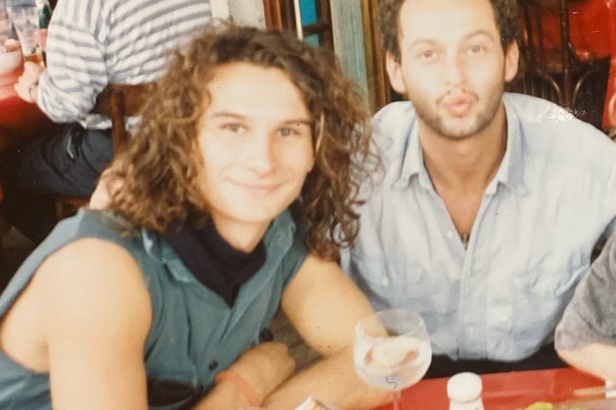 Three young people sit at a restaurant table smiling in a slightly blurry film photograph. 