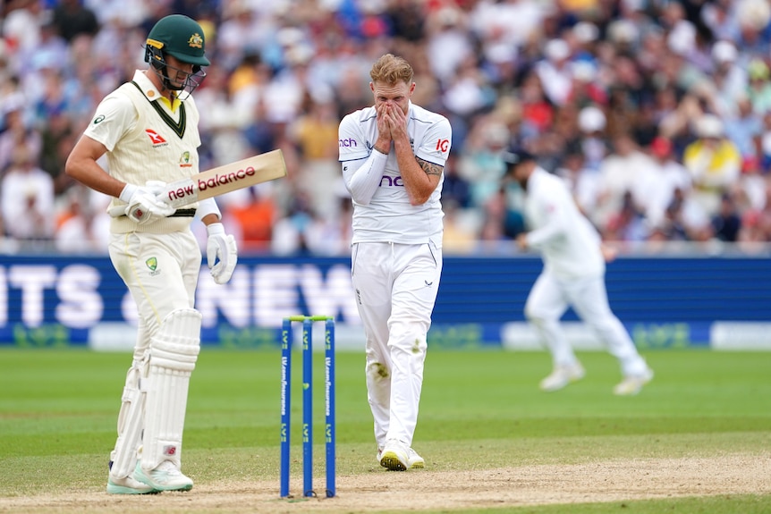Ben Stokes holds his head in his hands as Pat Cummins stands in the foreground.