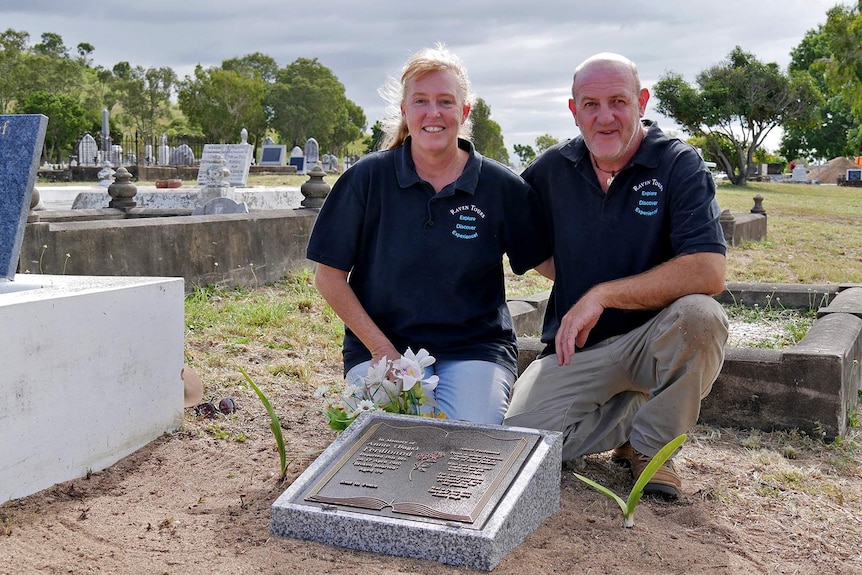 A man and woman kneel beside a memorial headstone at the Belgian Gardens Cemetery