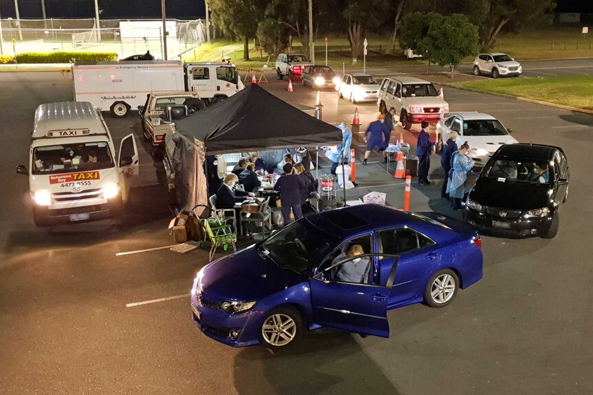 Cars queue next to a tent on an outdoor carpark.