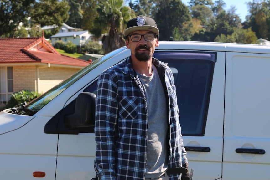 A builder stands in front of a van.