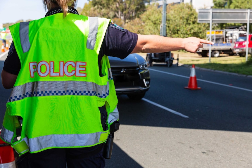 Queensland police officer directs cars at a border check point on the Gold Coast.