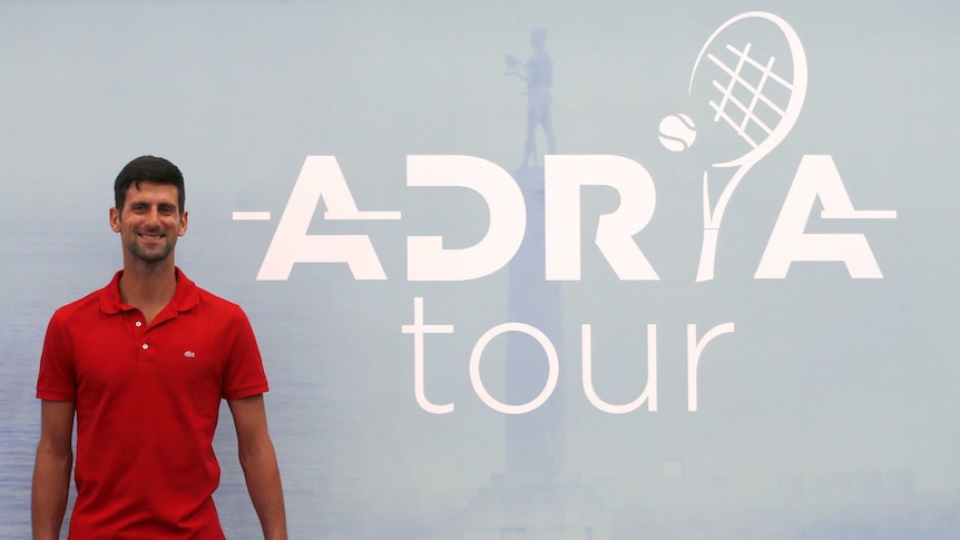 A tennis player smiles while standing next to the logo of his newly-announced tennis tour.