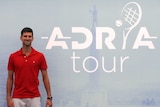 A tennis player smiles while standing next to the logo of his newly-announced tennis tour.