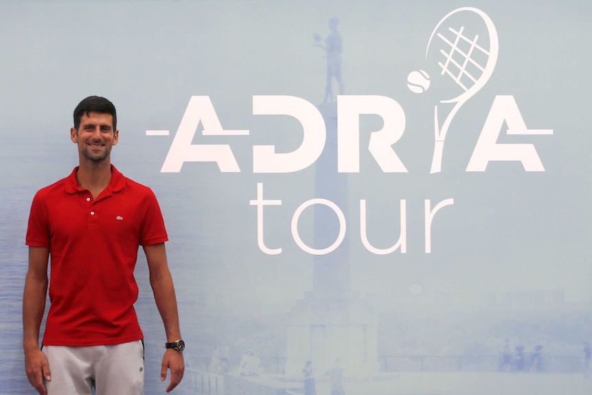 A tennis player smiles while standing next to the logo of his newly-announced tennis tour.
