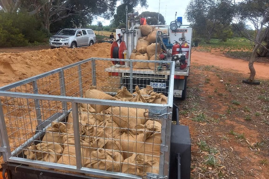 multiple filled sandbags in the back of a caged trailer attached to a vehicle.