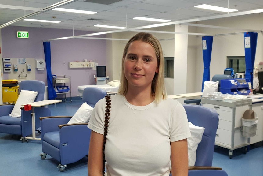 Alex Lewis wearing a white t-shirt, standing in a large hospital consulting room