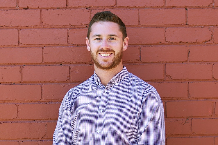 A man in a collared shirt stand in front of a red brick wall.