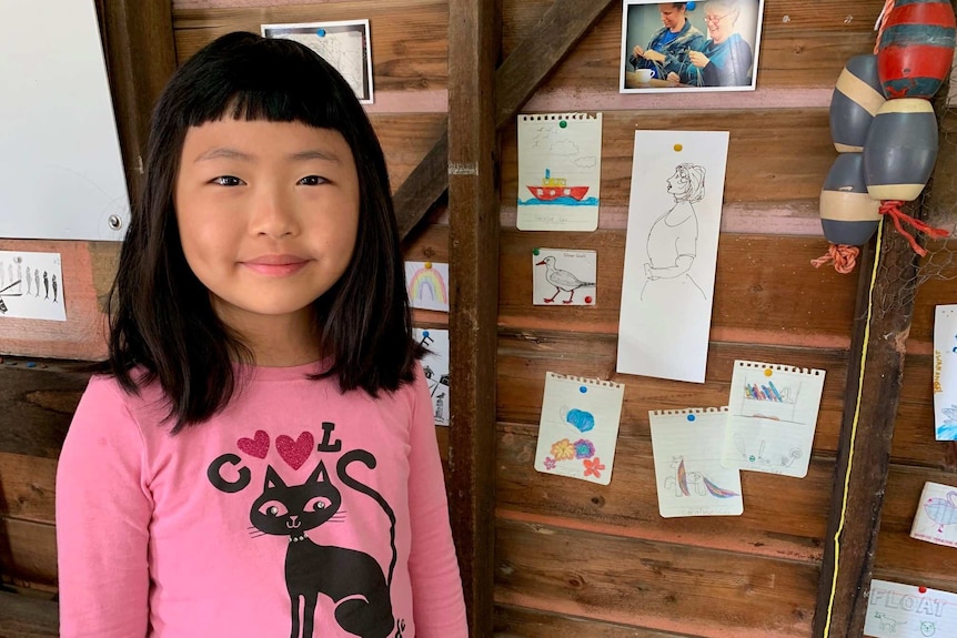 Young girl stands proudly by the picture of the sailing ship she had drawn.