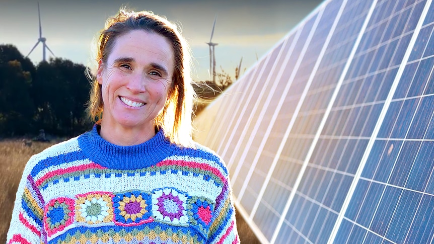 Dimity Taylor stands on her farm wearing a blue and white jumper next to a large solar panel.