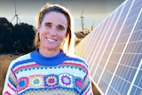 Dimity Taylor stands on her farm wearing a blue and white jumper next to a large solar panel.