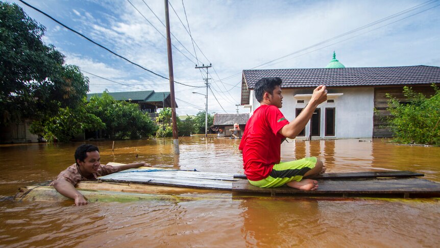 People use a makeshift raft to cross through a flooded village in Banjar, South Kalimantan on Borneo Island.