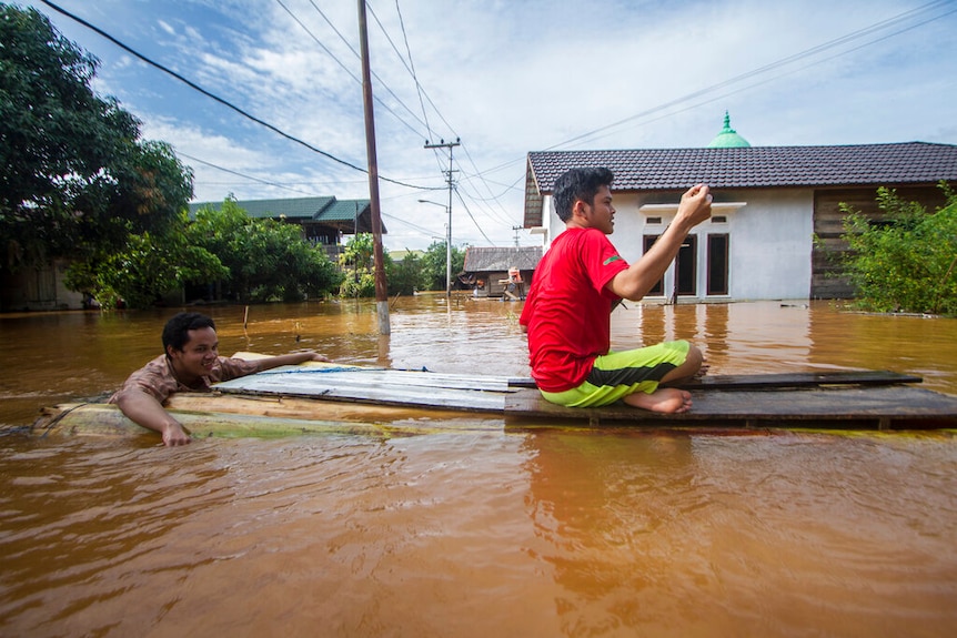 People use a makeshift raft to cross through a flooded village in Banjar, South Kalimantan on Borneo Island.