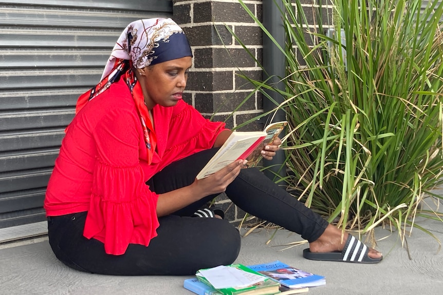 A woman wearing a headscarf sitting reading a book.