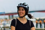 Michelle Mannering rides an e-scooter on a wharf wearing a helmet and smiling on a grey day.