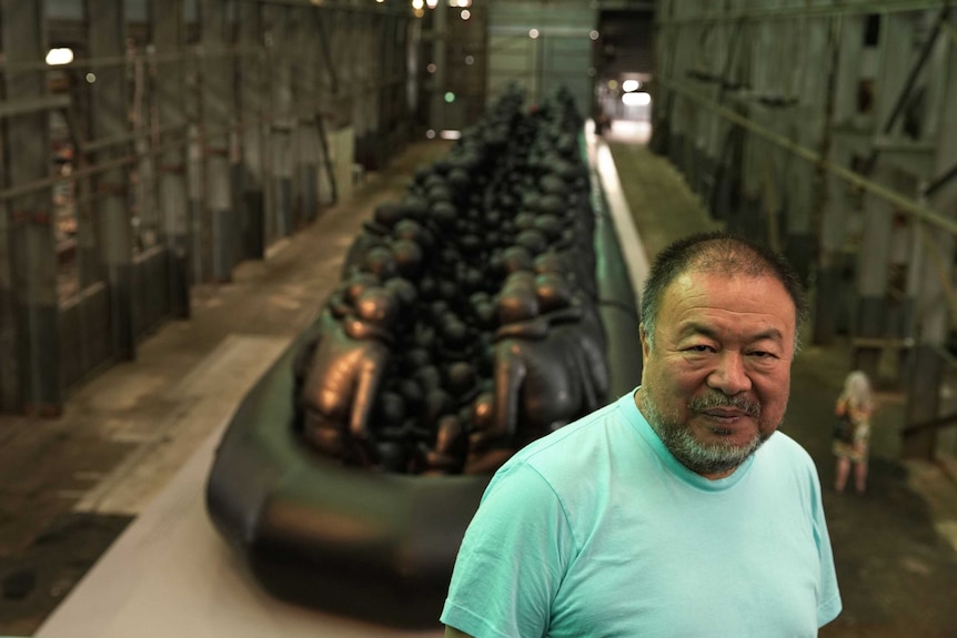 Ai Weiwei in front of his art installation which features a giant inflatable boat filled with people wearing life jackets