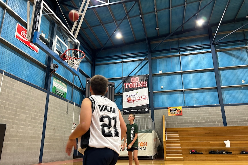 A young basketball player in a white jersey shooting hoops