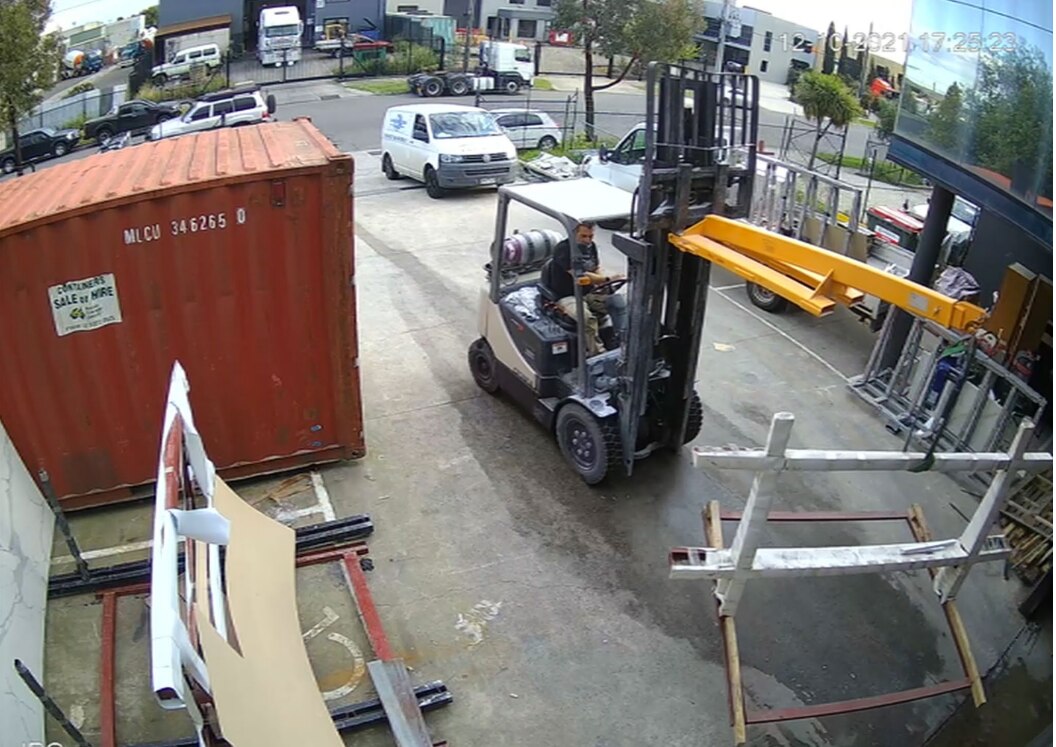 A man drives a forklift that is carrying three yellow poles surrounded by other metal.