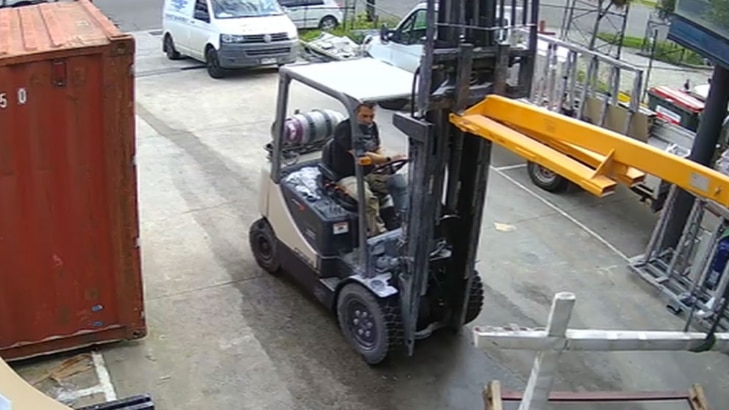 A man drives a forklift that is carrying three yellow poles surrounded by other metal.