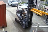 A man drives a forklift that is carrying three yellow poles surrounded by other metal.