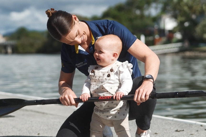 Alyce Wood and daughter Florence on a pier, holding a paddle, smiling.