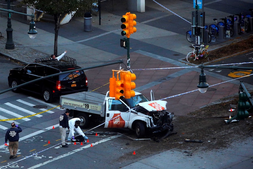 A burnt out ute sits under yellow traffic lights at intersection, police in white jumpsuits around it