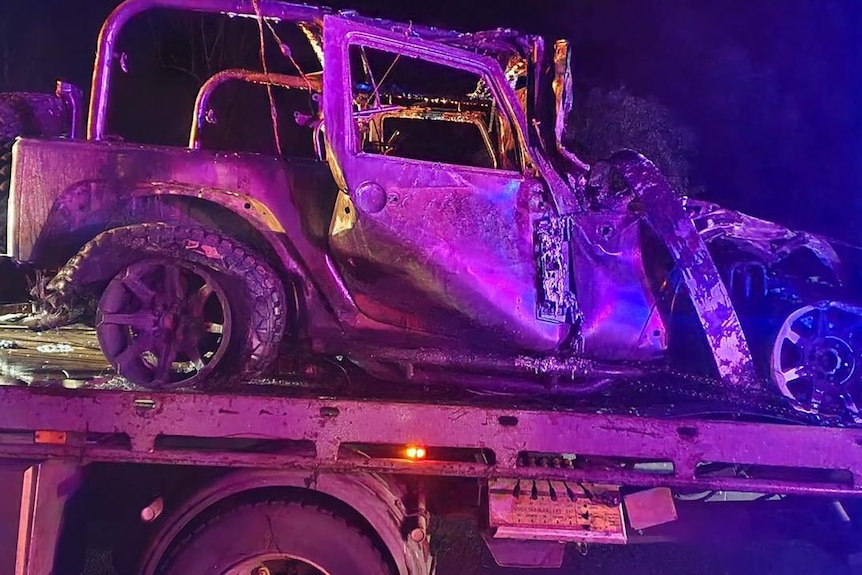 a burnt out Jeep on the back of a tow truck at night.
