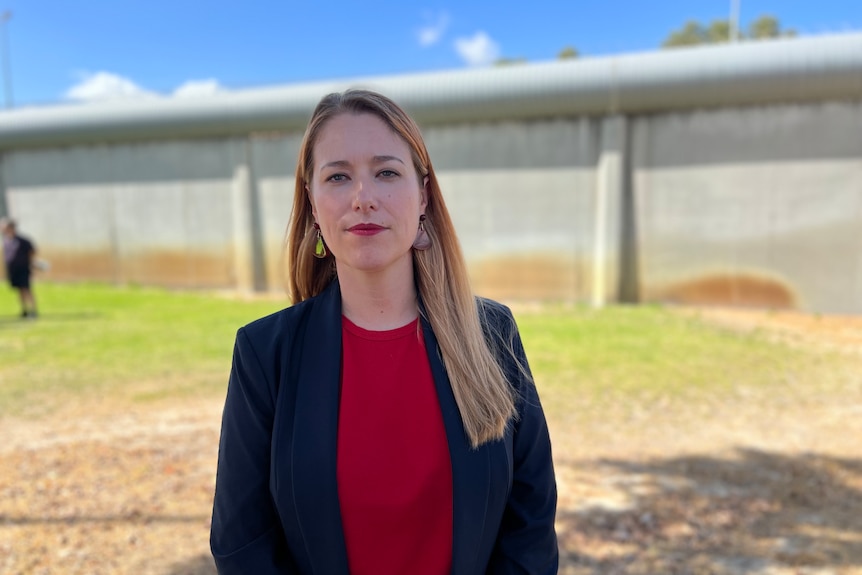 A woman wearing a read top and a dark blazer looks serious. 