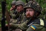 Three Ukrainian servicemen take rest, sitting on the ground. 