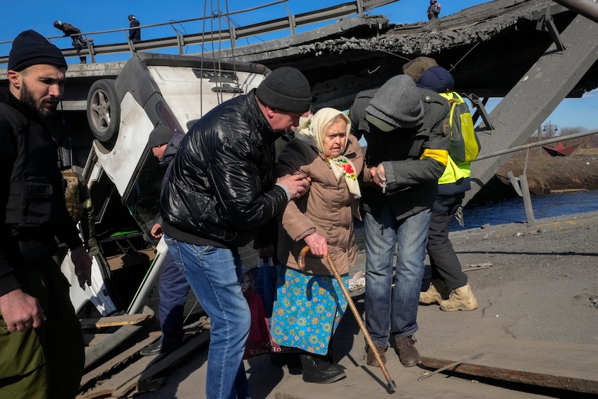 Volunteers pass an improvised path under a destroyed bridge as they evacuate an elderly resident in Irpin.
