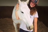 Olivia with a white horse, in her riding gear.