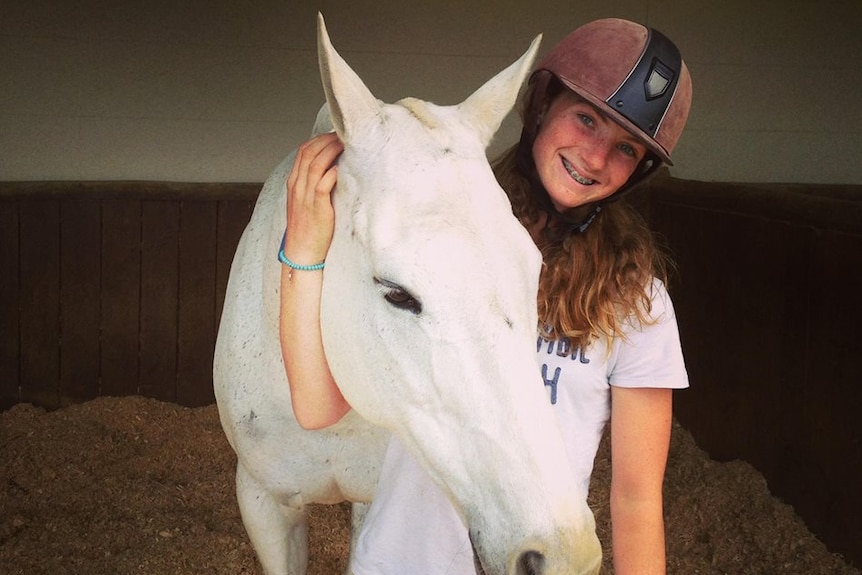 Olivia with a white horse, in her riding gear.