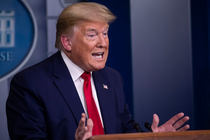 A man in a suit gestures as he speaks from behind a lecturn.