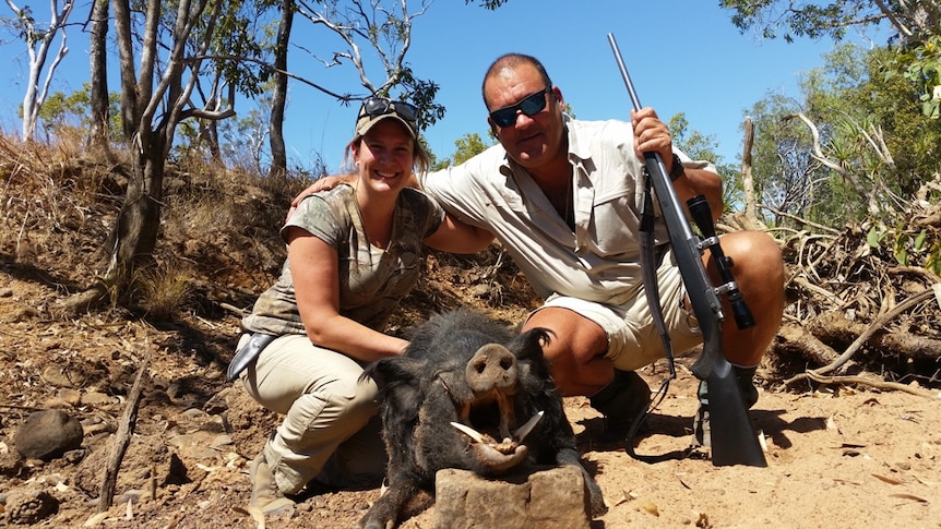 A woman and a man with a gun kneeling with a dead wild pig.