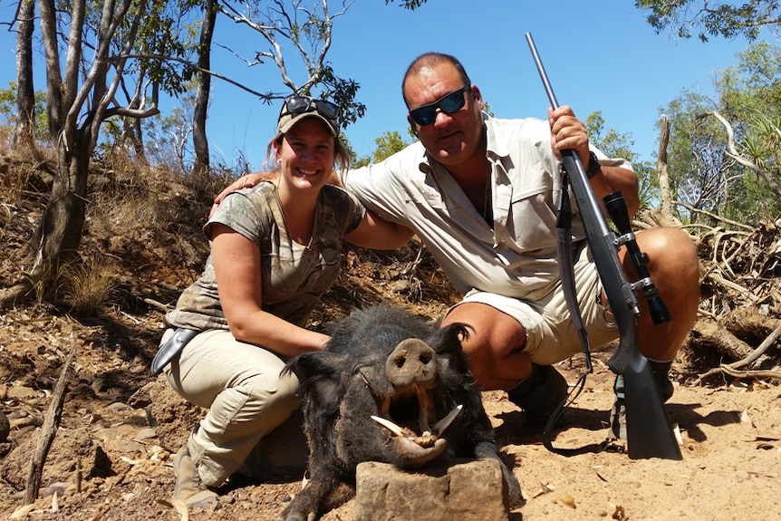 A woman and a man with a gun kneeling with a dead wild pig.