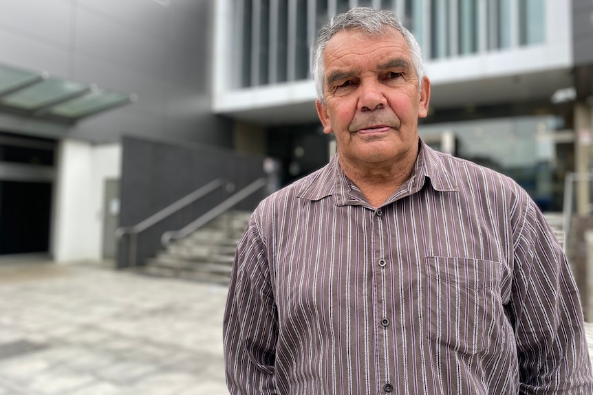 An elderly man standing outside court, looking serious.