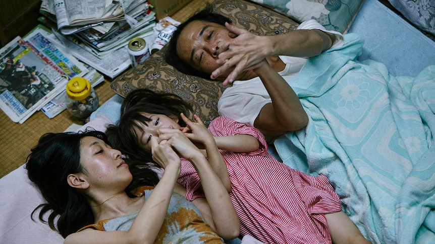 Two adults lay on mats the floor, with a young girl between them.