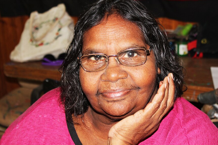 An Indigenous woman with glasses and a pink shirt looks to the camera.