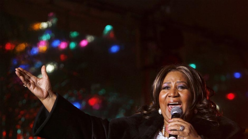 Aretha Franklin singing into a microphone with her arm out and palm upwards