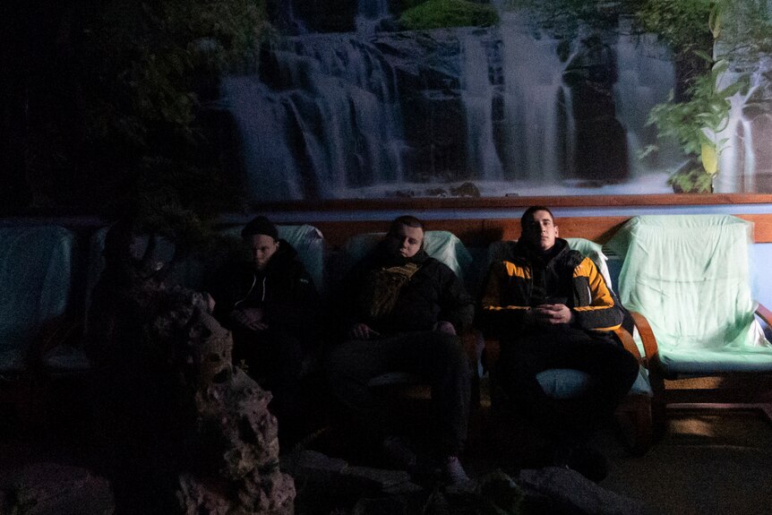 People rest with their eyes closed in a dark room with a waterfall mural.