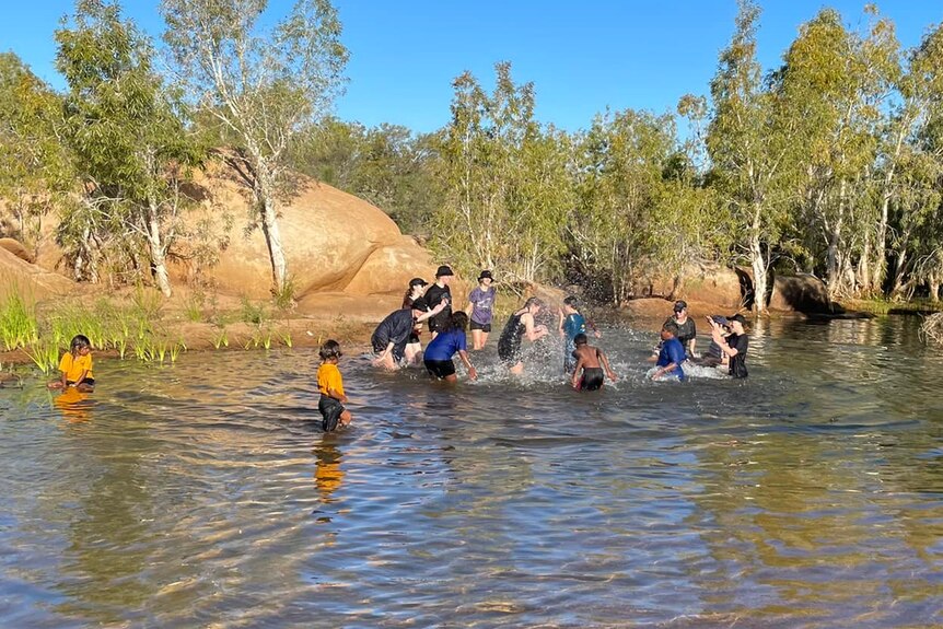 A group of students swim and splash eachother in a waterhole.