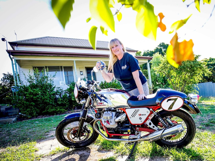 Tracy cleans her bike with a soapy cloth in the sunshine outside a weatherboard house