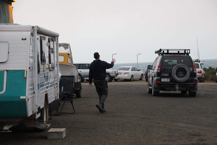 A man walks between a caravan and a four wheel drive which are parked at a jetty