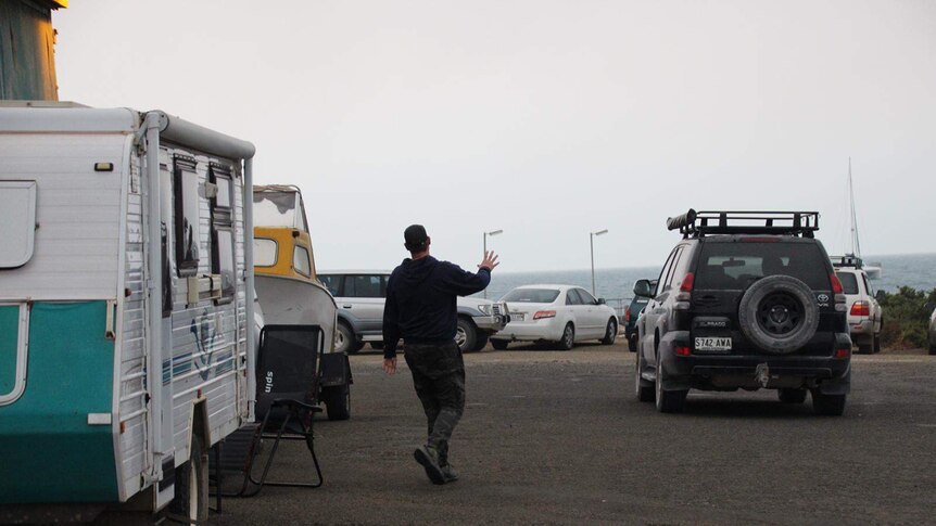 A man walks between a caravan and a four wheel drive which are parked at a jetty