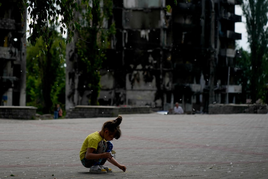 A girl plays at a square near buildings destroyed during attacks 