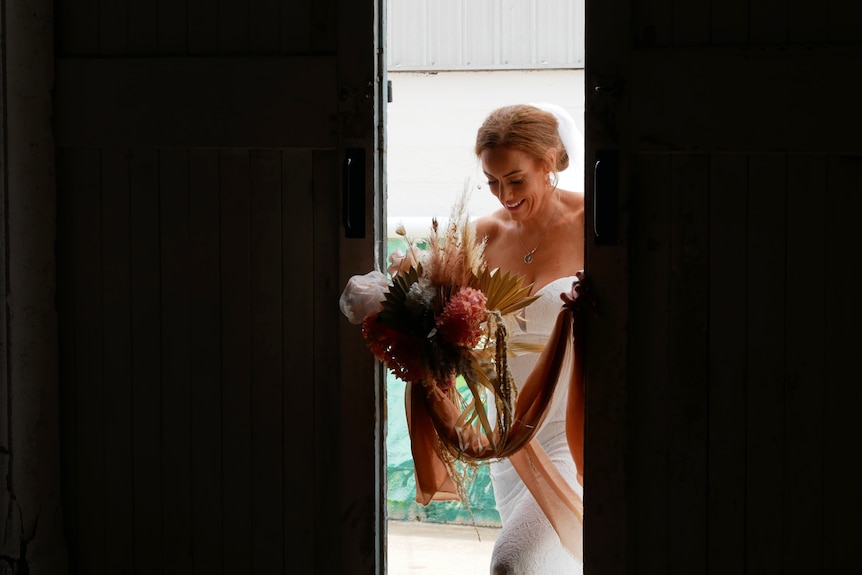 A bride carrying a bouquet prepares to walk through a doorway 