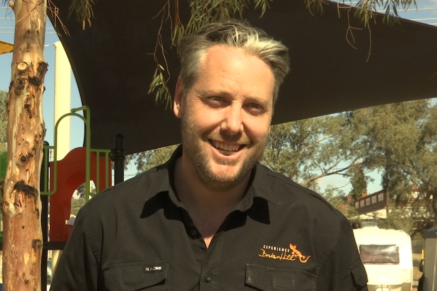 A man smiling in front of the camera at a caravan park wearing a black shirt