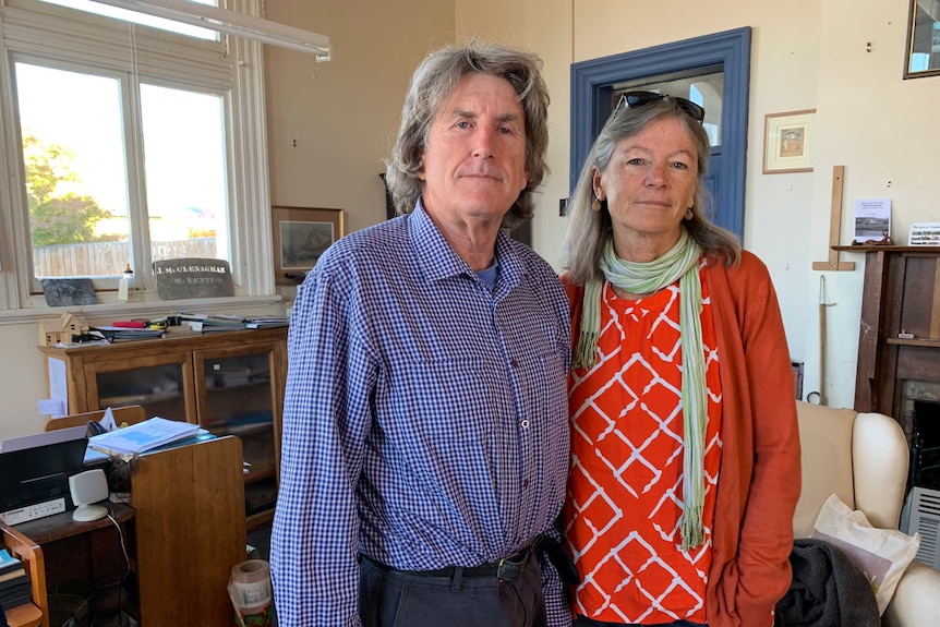 A man and a woman standing in their living room, with a window in the background